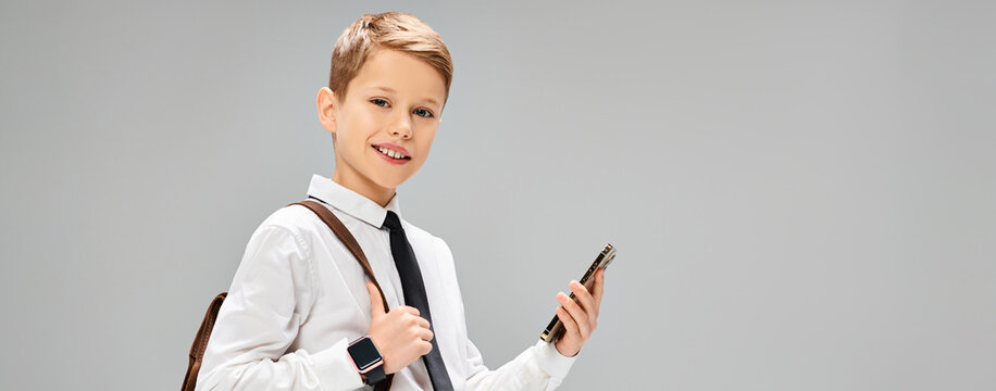 Cute little boy dressed in formal business attire with a smile holding a smartphone