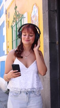 young latina girl or woman using headphones and listening music while holding mobile phone in public park in Mexico Latin America