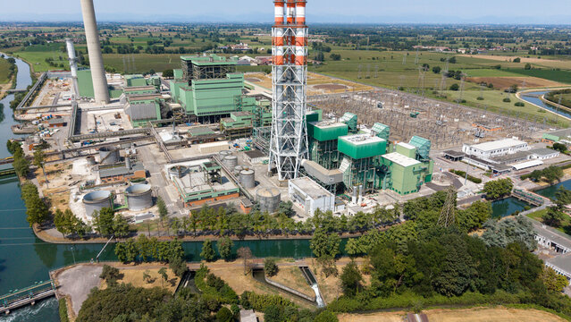 Aerial view of Stazione Elettrica TERNA - TAVAZZANO EST power plant with industrial chimneys, cooling towers, and electrical infrastructure near a canal in Montanaso Lombardo, Lombardia, Italy.