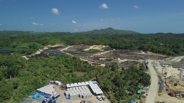 Aerial view of Sikatuna Solar Power Plant featuring rows of solar panels, construction materials, and surrounding lush green hills in Sikatuna, Central Visayas, Philippines.