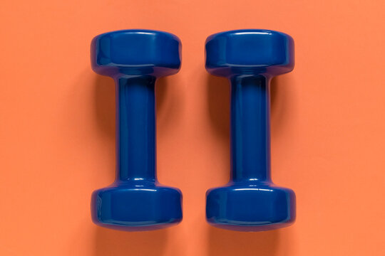 Minimal workout equipment on a bright orange background showcases blue dumbbells as a symbol of fitness, healthy living, strength building, and active daily routines.
