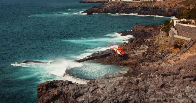 Medical helicopter landing on rocky volcanic shore for rescue operation. Aviation provides first aid to the injured. Stormy ocean beach.