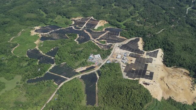 Aerial view of Sikatuna Solar Power Plant with rows of solar panels on cleared hilly terrain surrounded by lush tropical forest in Sikatuna, Central Visayas, Philippines.