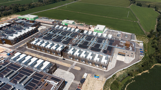 Aerial view of the Stack Infrastructure MIL04 Campus data center with industrial buildings, rooftop cooling units, and solar panels, surrounded by fields in Vellezzo Bellini, Lombardy, Italy.