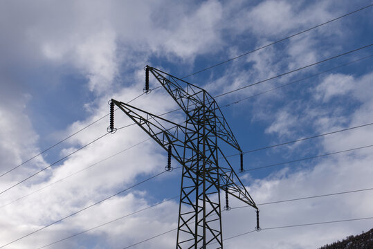 Metal power transmission pylon standing strong against a vivid blue sky filled with white fluffy clouds. High Voltage Electricity Pylon