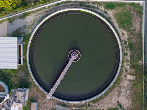 Aerial view of a circular wastewater treatment tank with a rotating bridge in an industrial facility in Chivasso, Piedmont, Italy.