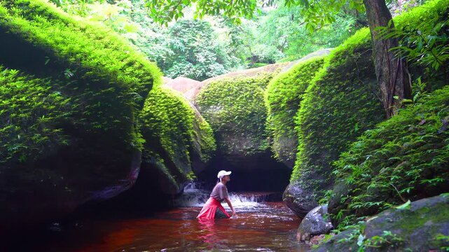 An Asian woman splashes water onto a dolphin-shaped rock at Phu Langka National Park, Bueng Kan Province, Thailand.