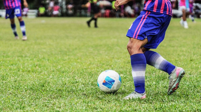 Football player dribbling the ball across grass field during competitive outdoor soccer game