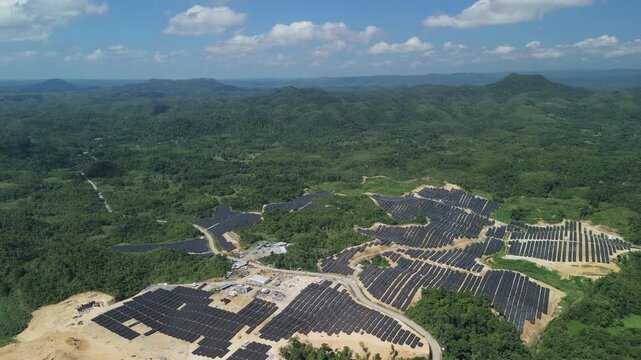 Aerial view of the Sikatuna Solar Power Plant featuring rows of photovoltaic panels set amidst lush green hills and forests in Sikatuna, Central Visayas, Philippines.