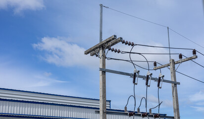 Electric power lines are seen on a wooden pole. The pole stands next to a building as clouds drift across the blue sky. The scene shows infrastructure for electricity © Happy Photo