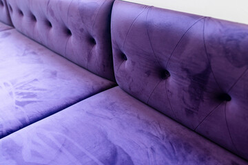 Fototapeta premium Close-up of a purple velvet tufted sofa with soft fabric texture. Modern interior furniture background, ideal for home decor, upholstery, luxury, and lifestyle design
