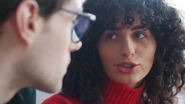 Young curly haired Caucasian woman talking with colleague during meeting. Close up of female sharing ideas while looking at coworker in glasses. Friendly teamwork and communication.