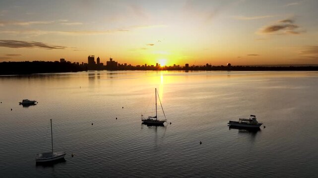 Aerial view of Matilda Bay at sunset with sailboats on the water and the Perth skyline in the distance in Crawley, Western Australia, Australia.