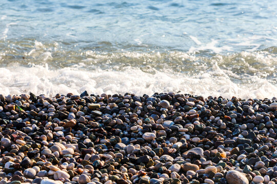 Sea wave washing pebble shore with large round stones, ocean water flowing rocky beach with smooth gray pebbles, coastal nature seascape.