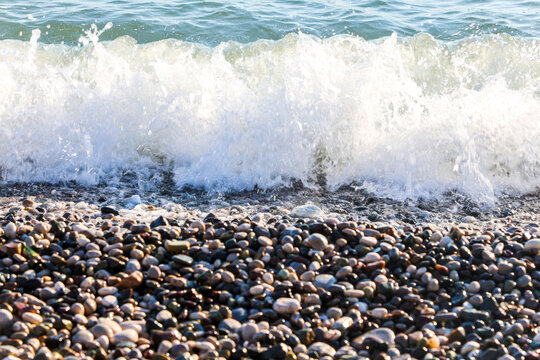 Sea wave washing pebble shore with large round stones, ocean water flowing over rocky beach with smooth gray pebbles, coastal nature seascape.