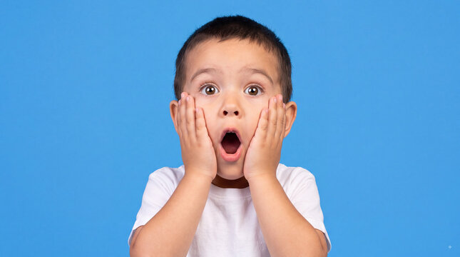 A young boy with a shocked expression on his face, hands on his cheeks, against a blue background