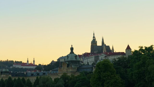 Historic Prague Castle and Saint Vitus Cathedral stand against a warm sunset sky. This iconic medieval hilltop fortress dominates the Czech capital city skyline at dusk during golden hour.