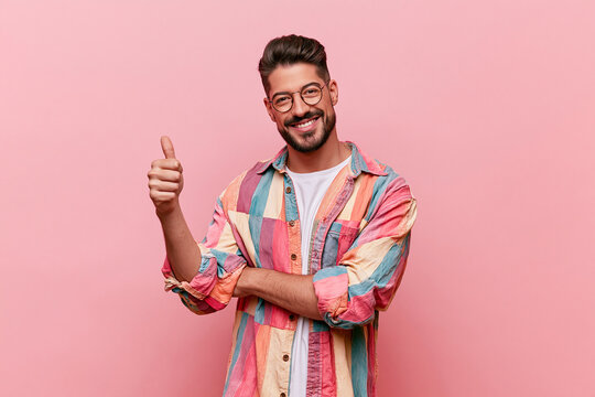 A portrait of a smiling man with glasses, a beard, and a multicolored shirt over a white shirt, set against a solid vivid background.