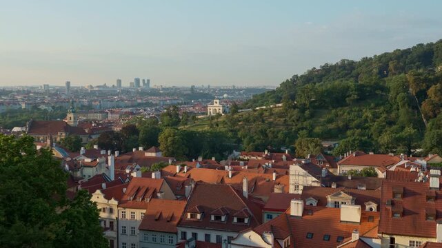 Prague city panorama showcases historic houses near green Petrin Hill. Old town architecture contrasts with distant modern skyscrapers at morning. Czechia landmark offers travel scenery.