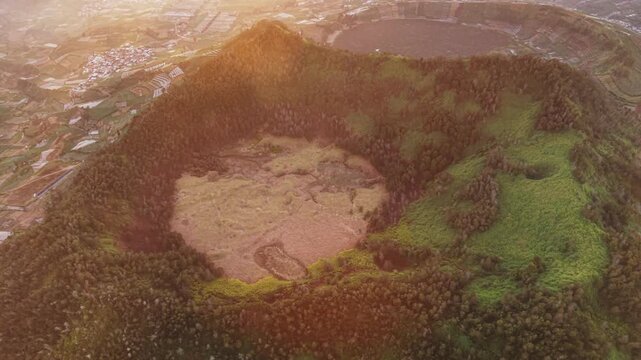 Aerial view of the volcanic crater at Dieng Plateau with lush green vegetation and surrounding agricultural fields during golden hour in Indonesia.
