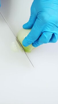 Professional chef hands in blue gloves slicing half onion close up on white kitchen cutting board. Minced with big iron knife. Cooking, preparing ingredients in restaurant. Top down view. 4k footage.