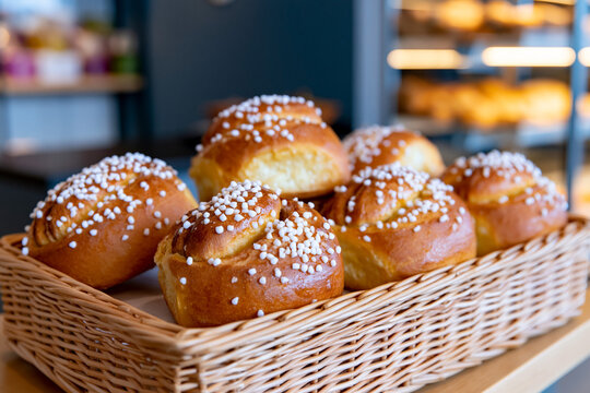 Freshly baked sweet rolls with sugar sprinkles arranged in a wicker basket on a wooden table, with blurred bakery items in the background