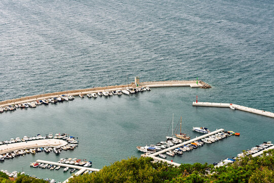 The curved breakwaters, lighthouses, and marina docks filled with docked boats and yachts at Ba&scaron;ka Harbor on the southern tip of Krk Island, Croatia, set against deep blue Adriatic Sea waters.