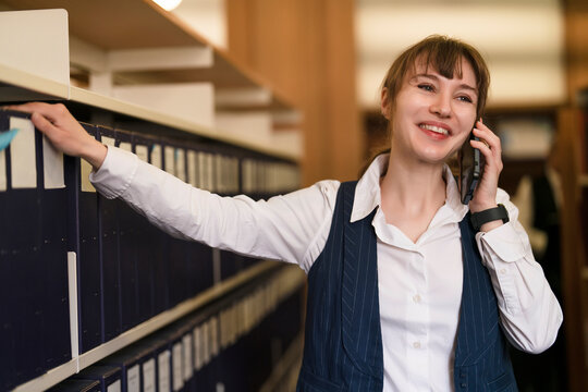 Woman talking on phone while standing by filing cabinets in an office setting
