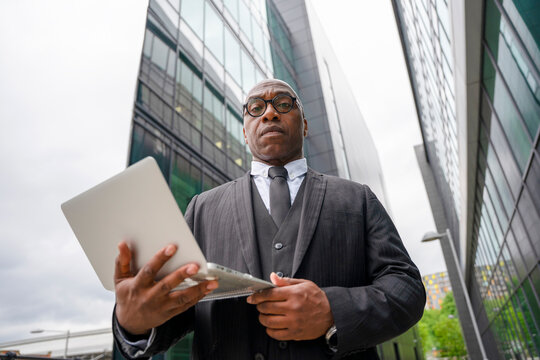 Businessman works on a laptop outside a modern building during a cloudy day in the city