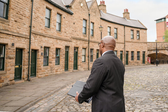 Man in a suit walks on a cobblestone street looking at buildings in an urban area during the day