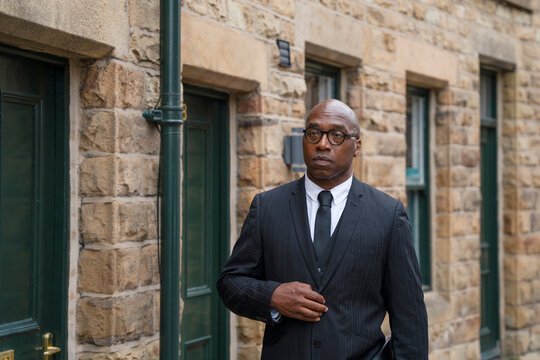 Businessman walking on a street near stone buildings during the day while adjusting his suit
