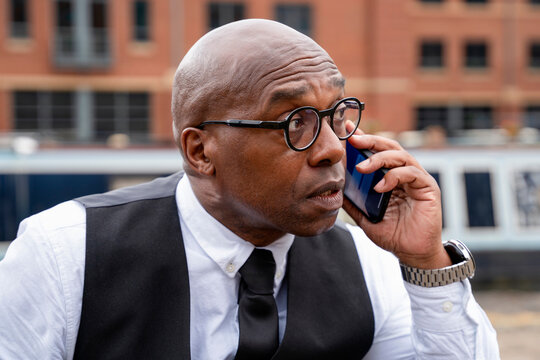 Man talking on phone by the water with buildings in the background during daytime