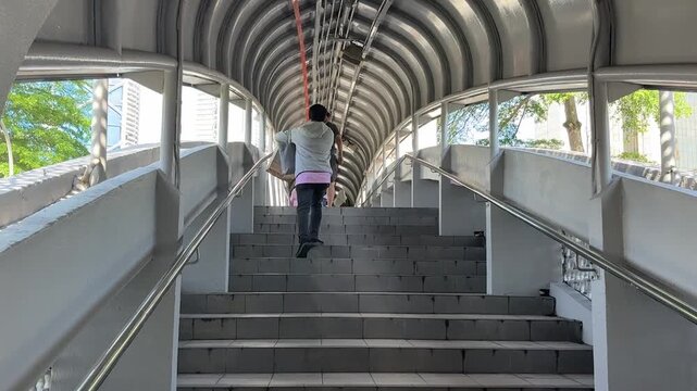 Daily commuters walking through modern pedestrian link bridge at KTM railway station in Kuala Lumpur city center.