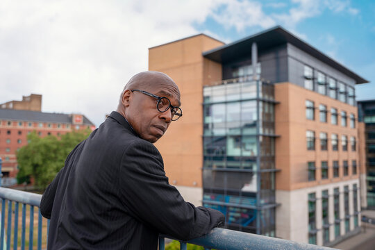 Man stands on balcony looking back at the modern buildings in the urban landscape under a partly cloudy sky