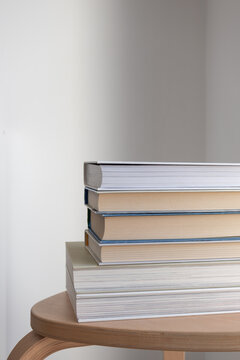 Stack of books on wooden side table in minimalist interior. Education, reading, learning, knowledge, and modern lifestyle, book club