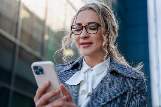 Woman looking at her smartphone while standing outside a modern building in a city