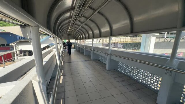 Daily commuters walking through modern pedestrian link bridge at KTM railway station in Kuala Lumpur city center.