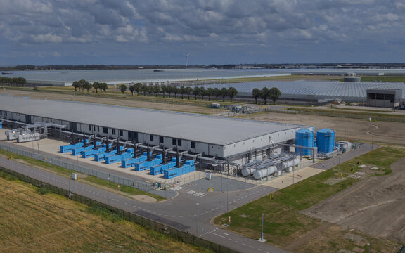 Aerial view of the Google data center Agriport A7 featuring large industrial buildings, blue cooling tanks, and surrounding agricultural landscape in Middenmeer, North Holland, Netherlands.
