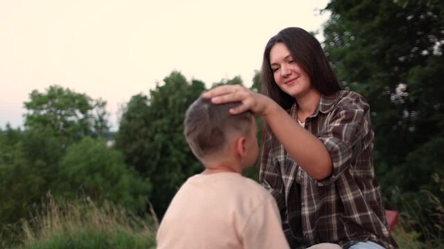 Mother gently strokes son head in close up slow motion. Nature background creates warm family moment with care and aff