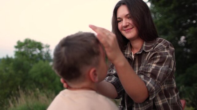 Mother gently strokes son head in close up slow motion. Nature background creates warm family moment with care and aff