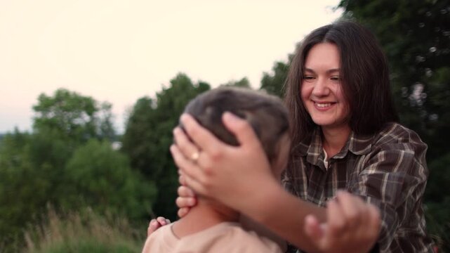 Mother gently strokes son head in close up slow motion. Nature background creates warm family moment with care and aff