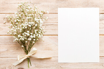 Fototapeta premium Wedding mockup with white paper list and flowers gypsophila on colored table top view flat lay. Blank greeting cards and envelopes. Beautiful floral pattern. Flat lay style