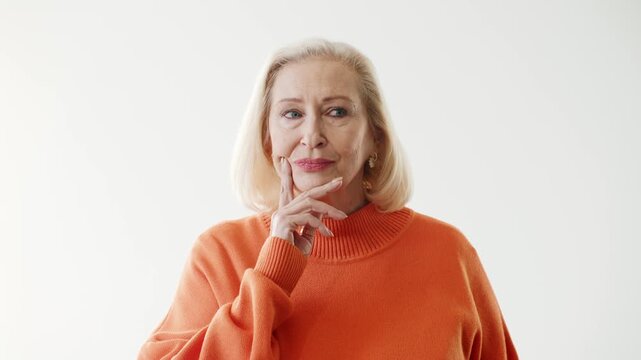 Thoughtful senior Caucasian woman touching chin while looking away and thinking. Elegant elderly female considering decision solving problem or planning. Clean studio background copy space.
