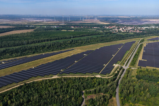Aerial view of the recultivated coal mines Leipziger Neuseenland featuring a large solar farm with rows of photovoltaic panels surrounded by forest and coal pits in Zwenkau, Saxony, Germany.