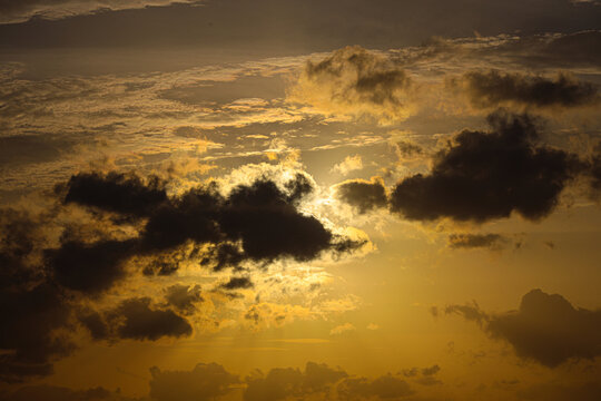 Sunlight breaks through dark storm clouds during a dramatic golden hour sunset in the open sky.
