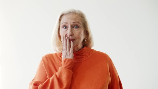 Senior Caucasian woman touching cheek with worried expression while looking upward. Elderly female reacting to toothache sudden pain or unexpected problem. Clean studio background copy space.