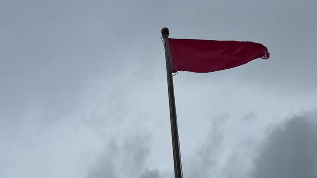 A striking red flag waves gently against a gray, cloudy sky, symbolizing resilience and strength in uncertain times.