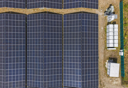 Aerial view of rows of solar panels in a solar farm with electrical equipment and storage units in Steenbergen, North Brabant, Netherlands.