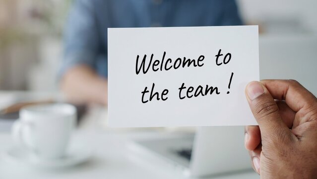Hand holding a white card with the handwritten text welcome to the team