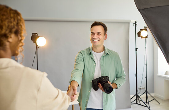 Photographer model handshake in studio with camera. Smiling model meets photographer by backdrop as portrait lighting glows and teamwork begins. Clear partnership message for hiring, booking.